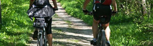 Zwei Personen auf Mountain Bikes die einen Wanderweg mit Ausrüstung am Fahrrad entlang fahren.