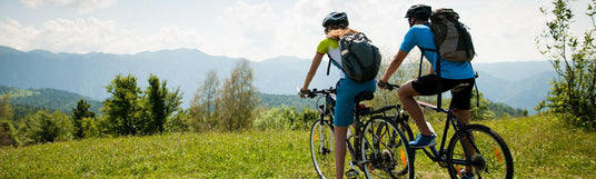Zwei Personen auf Mountain Bikes schauen ins weite Bergpanorama: Fahrradausrüstung mieten