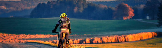 Person auf einem Fahrrad die am Waldrand einen Radweg entlang fährt. Dabei trägt sich Professionelle Mountain Bike Ausrüstung