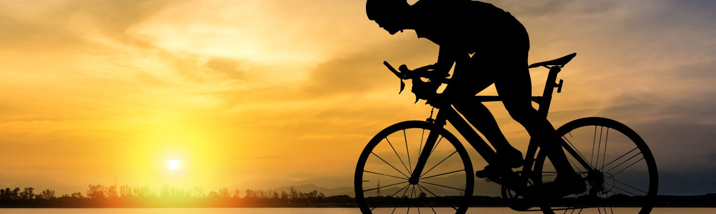 Mann auf Rennrad der an einem Fluss dem Sonnenuntergang entgegen fährt