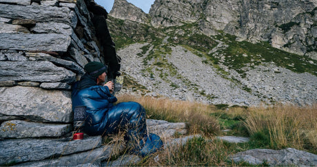 Man der auf einem Felsen mit seinem Blauen Schlafsack sitzt