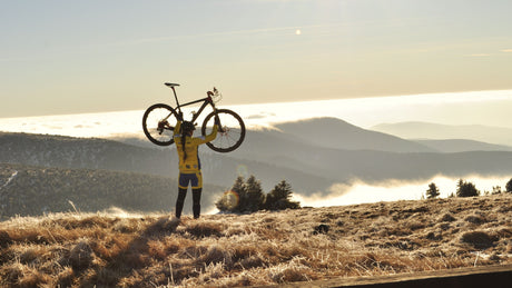 Mann hält sein Fahrrad in die Luft, vor Ihm das Bergpanorama: Fahrradausrüstung mieten