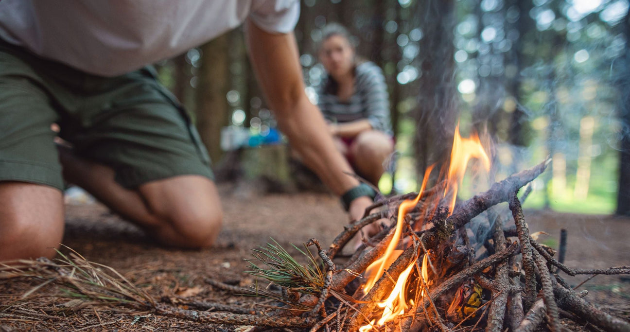 Nahaufnahme von Mann am Feuer im Hintergrund eine Frau: Abenteuer Kurse