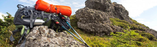 Rucksack mit einem Zelt befestigt liegen zusammen mit Wanderstöcken auf einem Stein