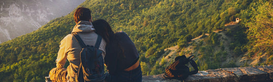 Pärchen sitzt auf einer Stein Mauer und schaut weit in die Ferne des Bergpanoramas