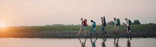 Kleine Gruppe von Wanderern läuft an einem Fluss entlang und die Sonne geht unter