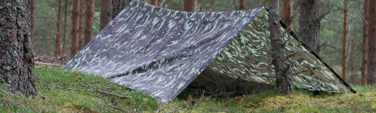 Camo-Tarp tief auf dem Waldboden abgespannt und ein Schlafsack ist darunter