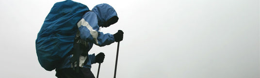 Ein Wandere gekleidet in Regenkleidung, Raincover über dem Rucksack und Stöcke in der Hand, wandert durch Nebel