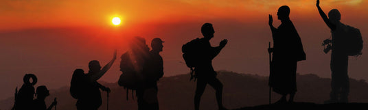 Gruppe von Wanderern freut sich bei Sonnenuntergang auf einem Gipfel angekommen zu sein, wo sie schon ein Mönch erwartet.