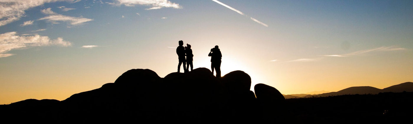 Gruppe Menschen steht während eines Sonnenuntergangs auf steinen und beobachten diesen: Wanderausrüstung mieten