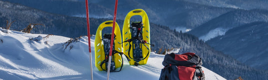 Schneeschuhe, Stöcke und ein Rucksack stecken im Schnee vor einer Bergpanorama Aussicht